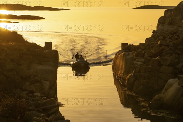 Motorboat with two persons sailing in harbour entrance at sunset, archipelago, Smögen, Smögenbryggan, Västra Götalands Län, Bohuslän, Sweden