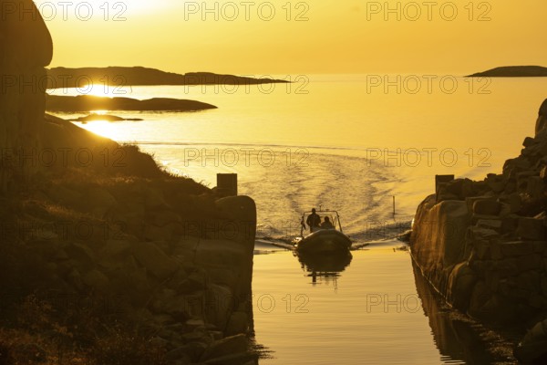 Motorboat with two persons sailing in harbour entrance at sunset, archipelago, Smögen, Smögenbryggan, Västra Götalands Län, Bohuslän, Sweden