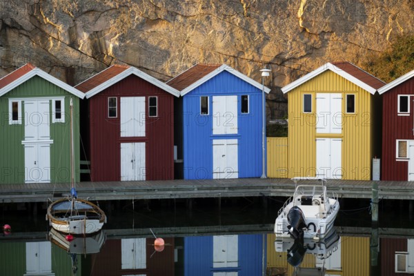 Colourful boathouses and boats in the calm water in front of rocks in the harbour of Smögen, Smögenbryggan, Västra Götalands Län, Bohuslän, Sweden