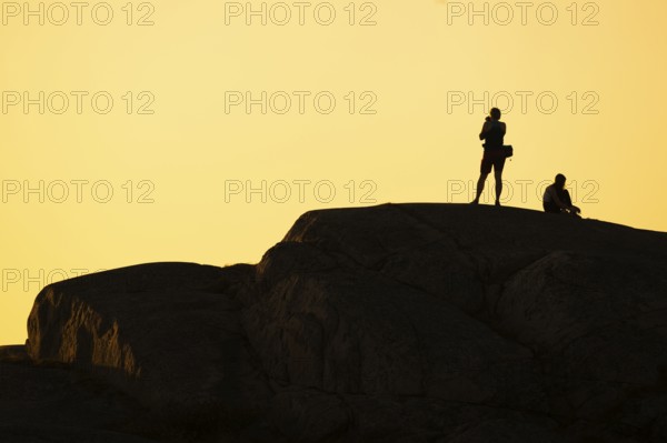 Silhouette of two tourists photographing the sunset on a rock, Smögen, Smögenbryggan, Västra Götalands Län, Bohuslän, Sweden