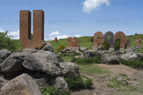Row of stone columns with motifs, integrated into a rocky, green landscape under a blue sky, monument to the Armenian alphabet, Aparan, Aragazotn Province, Armenia