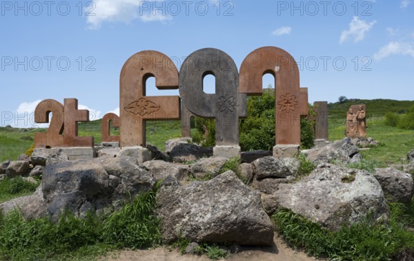 Stone pillars with traditional motifs, surrounded by large rocks and green grass, monument to the Armenian alphabet, Aparan, Aragazotn Province, Armenia
