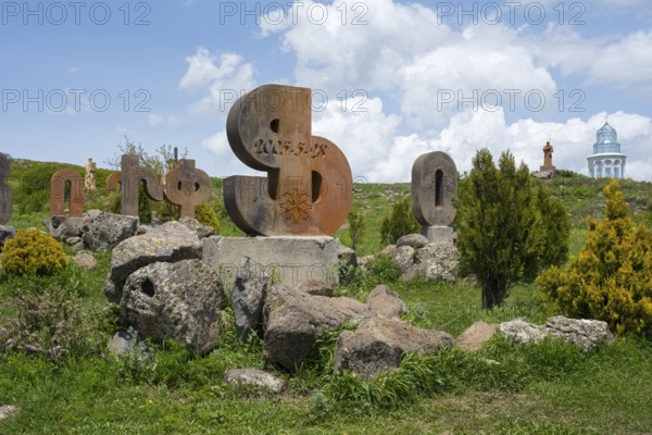 Stone sculptures in the shape of letters on a green meadow, surrounded by rocks and bushes under a cloudy sky, monument to the Armenian alphabet, Aparan, Aragazotn Province, Armenia