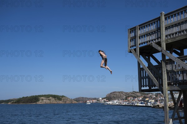 Girl jumping from a high wooden diving platform into the sea, lido, Fjällbacka, Bohuslän, West Sweden, Sweden