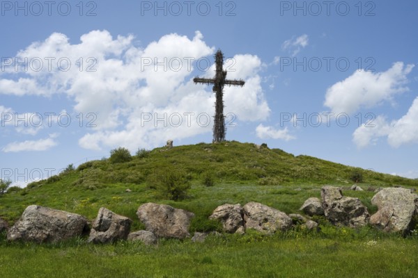 Metal cross on a green hill under a blue sky, surrounded by large stones, Monument to the Holy Cross, consisting of many small metal crosses, Aparan, Aragazotn, Armenia