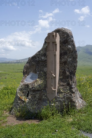 Stone with cross relief in front of a vast green landscape and blue sky, at the Monument of the Holy Cross, Aparan, Aragazotn Province, Armenia