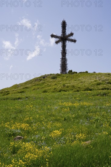 Large metal cross on a hill with a green meadow and yellow flowers under a blue sky, Monument to the Holy Cross, consisting of many small metal crosses, Aparan, Aragazotn Province, Armenia