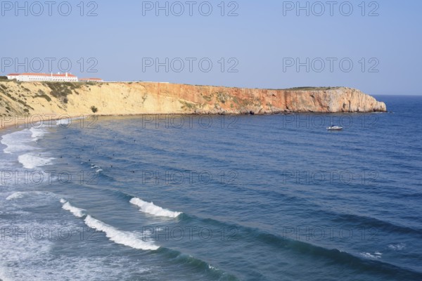 Cliffs with the Hotel Pousada de Sagres and surfers in the sea, Praia da Mareta, Sagres, Algarve, Portugal