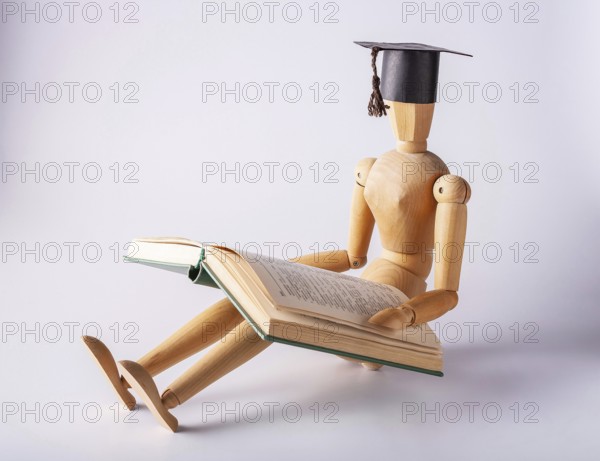 Wooden man in a student cap sits on the floor and reads a book, copy space