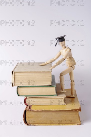 A wooden man in a student cap climbs up steps made from textbooks