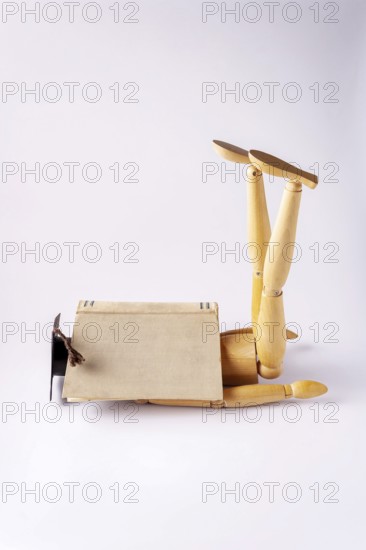 A wooden man in a student cap is tired and sleeping on the floor under an open book, copy space