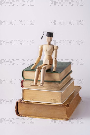 A wooden man in a student cap sits on a stack of textbooks on a white background