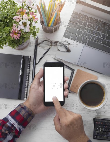 A person is using a cell phone on a desk with a laptop and a cup of coffee. The desk is cluttered with various items such as pens, pencils, and a calculator. Concept of productivity and focus, AI generated