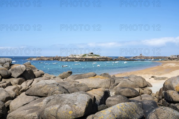 The wide bay of Tregastel on the Cote de Granit Rose shows the turquoise blue sea with white sailing boats and the characteristic round pink granite rocks, framed by large boulders in the foreground, Tregastel, Cotes-d'Armor department, Brittany region, France
