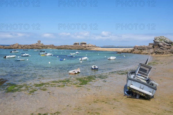 On the harbour beach of Tregastel on the Cote de Granit Rose, small boats lie on the light sand at low tide against the backdrop of the iconic pink granite rocks, Tregastel, Cotes-d'Armor department, Brittany region, France