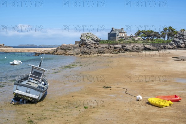 On the harbour beach of Tregastel on the Cote de Granit Rose, small boats lie on the light sand at low tide against the backdrop of the iconic pink granite rocks and Breton houses, Tregastel, Cotes-d'Armor department, Brittany region, France