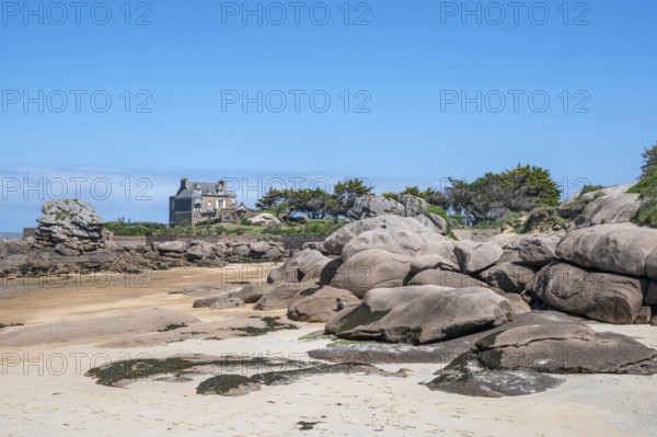 View from the harbour beach of Trégastel on the Côte de Granit Rose at low tide over the iconic pink granite rocks to a typical Breton house with granite façade and slate roof, Tregastel, Cotes-d'Armor department, Brittany region, France