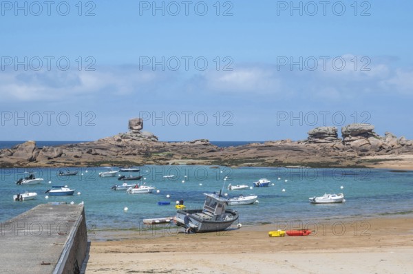 On the harbour beach of Tregastel on the Cote de Granit Rose, small sailing boats are moored next to the pier at low tide on the light-coloured sand against the backdrop of the iconic pink granite rocks r, Tregastel, Cotes-d'Armor department, Brittany region, France
