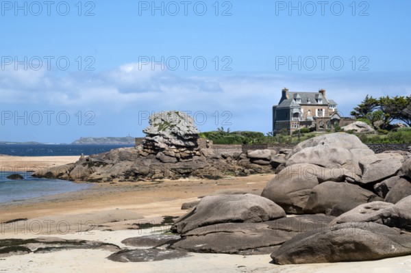 View from the harbour beach of Trégastel on the Côte de Granit Rose at low tide over the iconic pink granite rocks to a typical Breton house with granite façade and slate roof, Tregastel, Cotes-d'Armor department, Brittany region, France