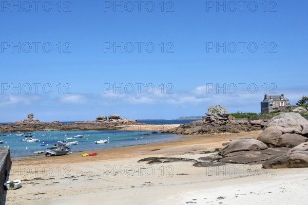 On the harbour beach of Tregastel on the Cote de Granit Rose, small sailing boats lie on the light sand at low tide against the backdrop of the iconic pink granite rocks and Breton houses, Tregastel, Cotes-d'Armor department, Brittany region, France