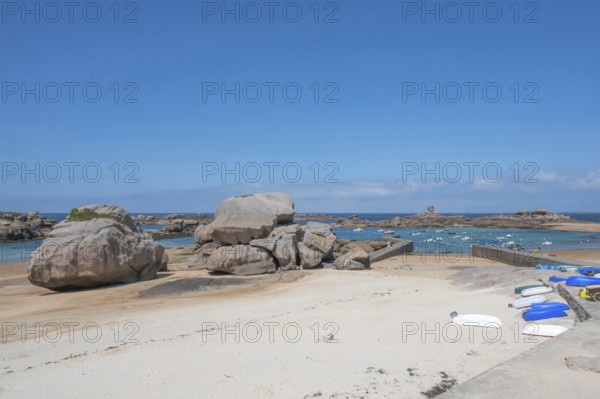 On the harbour beach of Trégastel on the Côte de Granit Rose, small boats lie on the light sand at low tide against the backdrop of the iconic pink granite rocks, Tregastel, Cotes-d'Armor department, Brittany region, France