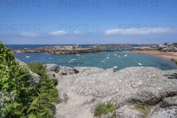 View from the GR 34 coastal hiking trail of the extensive sandy beach of the Plage de la Grève Rose on the Cote de Granit Rose with anchored boats, framed by the characteristic rounded pink granite rocks, Tregastel, Cote-d'Armor department, Brittany region, France