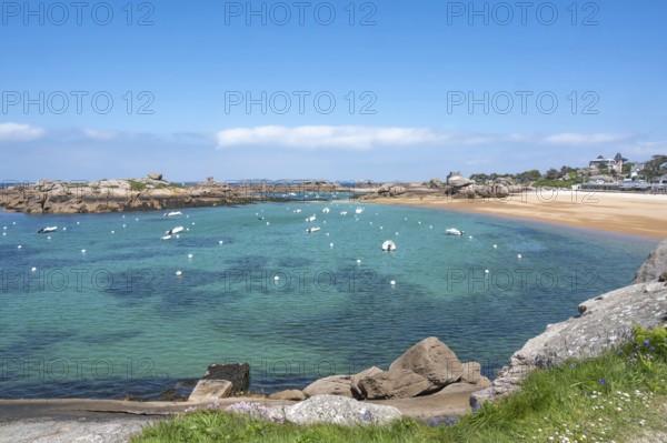View from the GR 34 coastal hiking trail of the extensive sandy beach of the Plage de la Greve Rose on the Cote de Granit Rose with anchored boats and buoys, framed by the characteristic rounded pink granite rocks, Tregastel, Cote-d'Armor department, Brittany region, France