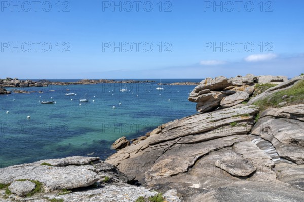 View from the GR 34 coastal hiking trail of the extensive sandy beach of the Plage de la Greve Blanche on the Cote de Granit Rose with anchored boats and buoys, framed by the characteristic rounded pink granite rocks, Tregastel, Cote-d'Armor department, Brittany region, France