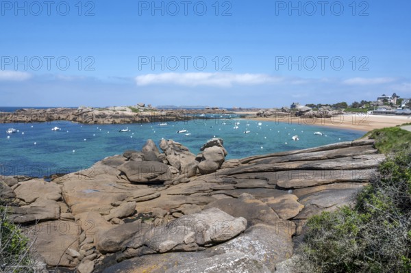 View from the GR 34 coastal hiking trail of the extensive sandy beach of the Plage de la Greve Rose on the Cote de Granit Rose with anchored boats and buoys, framed by the characteristic rounded pink granite rocks, Tregastel, Cote-d'Armor department, Brittany region, France