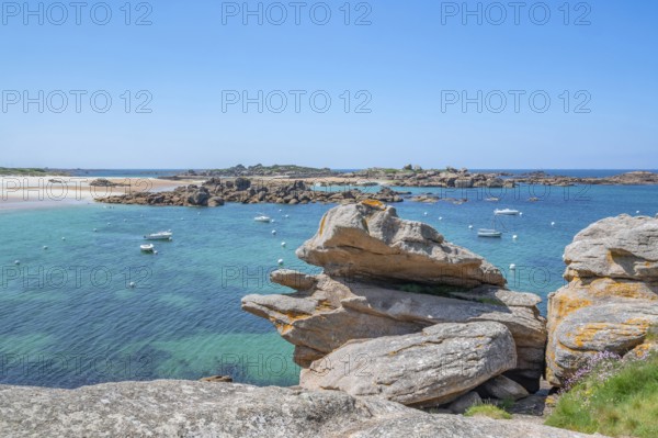 View from the GR 34 coastal hiking trail of the extensive sandy beach of the Plage de la Greve Blanche on the Cote de Granit Rose with anchored boats and buoys, framed by the characteristic rounded pink granite rocks, Tregastel, Cote-d'Armor department, Brittany region, France