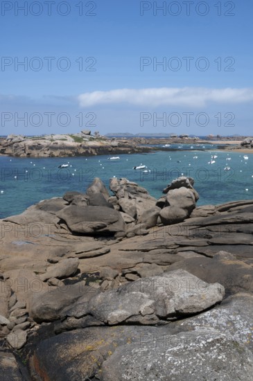 A picturesque coastal view of the pink granite coast near Tregastel shows the bay with the turquoise blue sea framed by striking pink-brown granite rocks, with large, weathered boulders in the foreground, Tregastel, Cote de Granit Rose, Cotes-d'Armor department, Brittany region, France