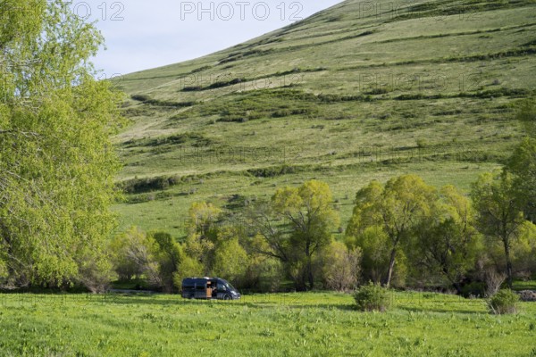 A black van stands in a green spring landscape in front of a gentle hill in the background, camper, landscape near Goghovit, Shirak province, Shirak, Armenia