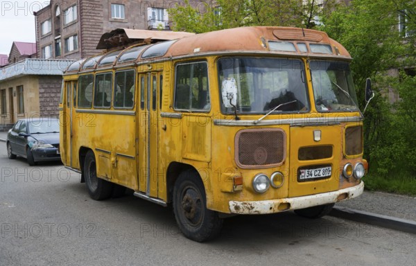 An old yellow bus stands abandoned on the street in an urban environment, clear signs of use, PAZ-672, minibus of the Soviet manufacturer Pavlovsky, Armenia
