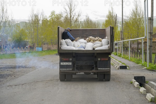 A lorry full of sacks is driven along a city street by a man in the back, exhaust fumes, Armenia