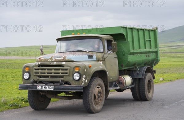 A green lorry with visible signs of wear driving on a country road in rural surroundings, ZIL-130 lorry, Armenia