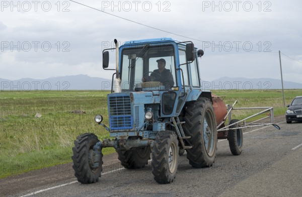 A blue tractor is driven by a man on a country road with fields and cloudy sky, Belarus MTZ-82 tractor or MTS-82, Armenia