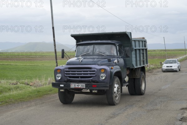 A blue lorry with a trailer drives on a country road surrounded by green fields and mountains, ZIL-130 lorry, Armenia