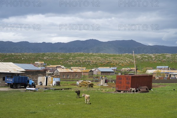 Rural settlement with huts and animals on a green pasture surrounded by mountains under a cloudy sky, Shenkani village, Aragazotn province, Armenia