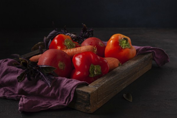 Peppers, tomatoes, carrots lie in a wooden box dark photo