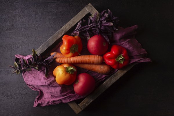 Orange and red vegetables on a red napkin in a wooden box dark photo