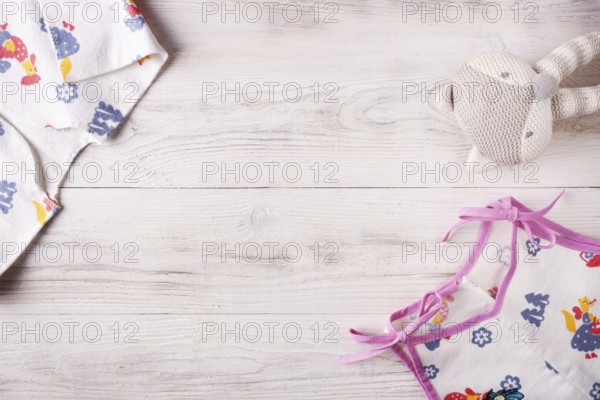 Clothes for a newborn and a rattle on a white wooden background