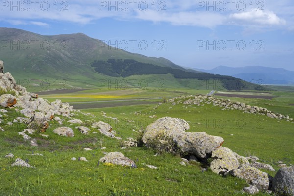 Green hilly landscape with rocks and mountains in the background under a slightly cloudy sky, landscape near Rya Taza with a view of the M3, Ria Taza, Aragatsotn province, Armenia