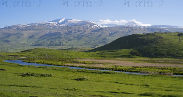 A wide view over a green valley with snow-capped mountains under a clear sky, landscape near Rya Taza with a view of the Aragaz, Ria Taza, Aragatsotn Province, Armenia