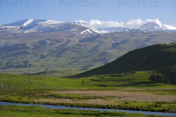 Snow-capped mountains rise above a green valley while the sky is clear and blue, landscape near Rya Taza with a view of the Aragaz, Ria Taza, Aragatsotn Province, Armenia
