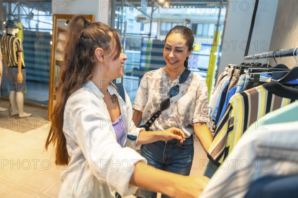 Two female customers smiling and chatting while selecting fashionable clothes in a vibrant retail store, enjoying their shopping experience together