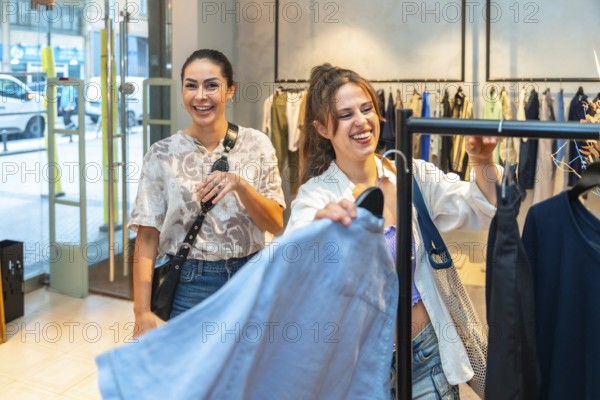 Two joyful female customers laughing and enjoying the experience of searching for trendy clothes in a vibrant, modern clothing store