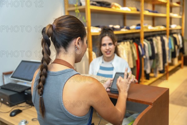 Customer making a contactless payment with her smartphone in a clothing store, assisted by the saleswoman