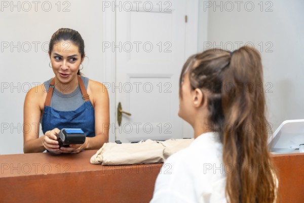 Smiling shop assistant holding a pos terminal for a customer making a contactless payment in a clothing store