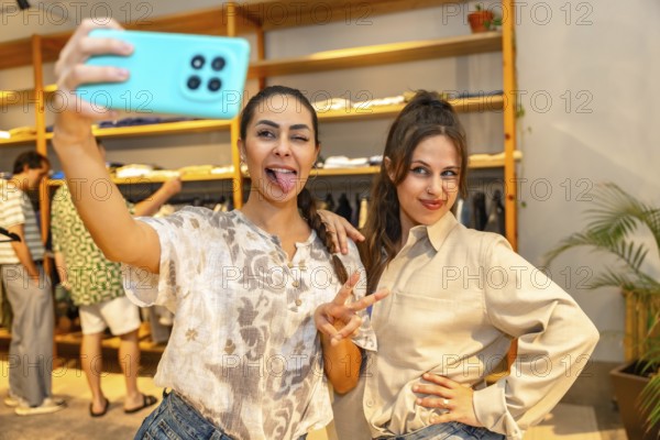 Two friends are having fun taking a selfie with a smartphone, sticking out their tongues, in a clothing store