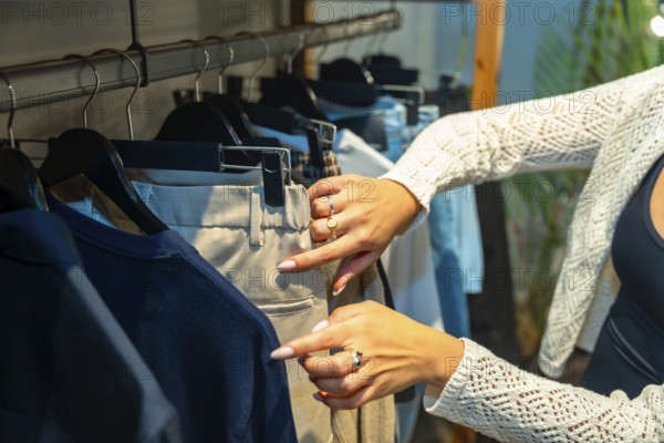 Female customer browsing through new collection in clothing store, selecting beige pants hanging on rack